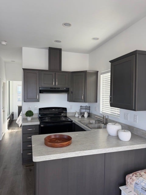 Modern kitchen with dark cabinets, black appliances, light countertops, a double sink, and minimal decor including white canisters and a wooden tray on the counter.