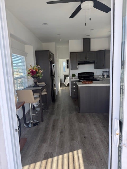 A view into a modern kitchen with gray cabinets, a small dining table with chairs, and a bedroom visible at the far end.