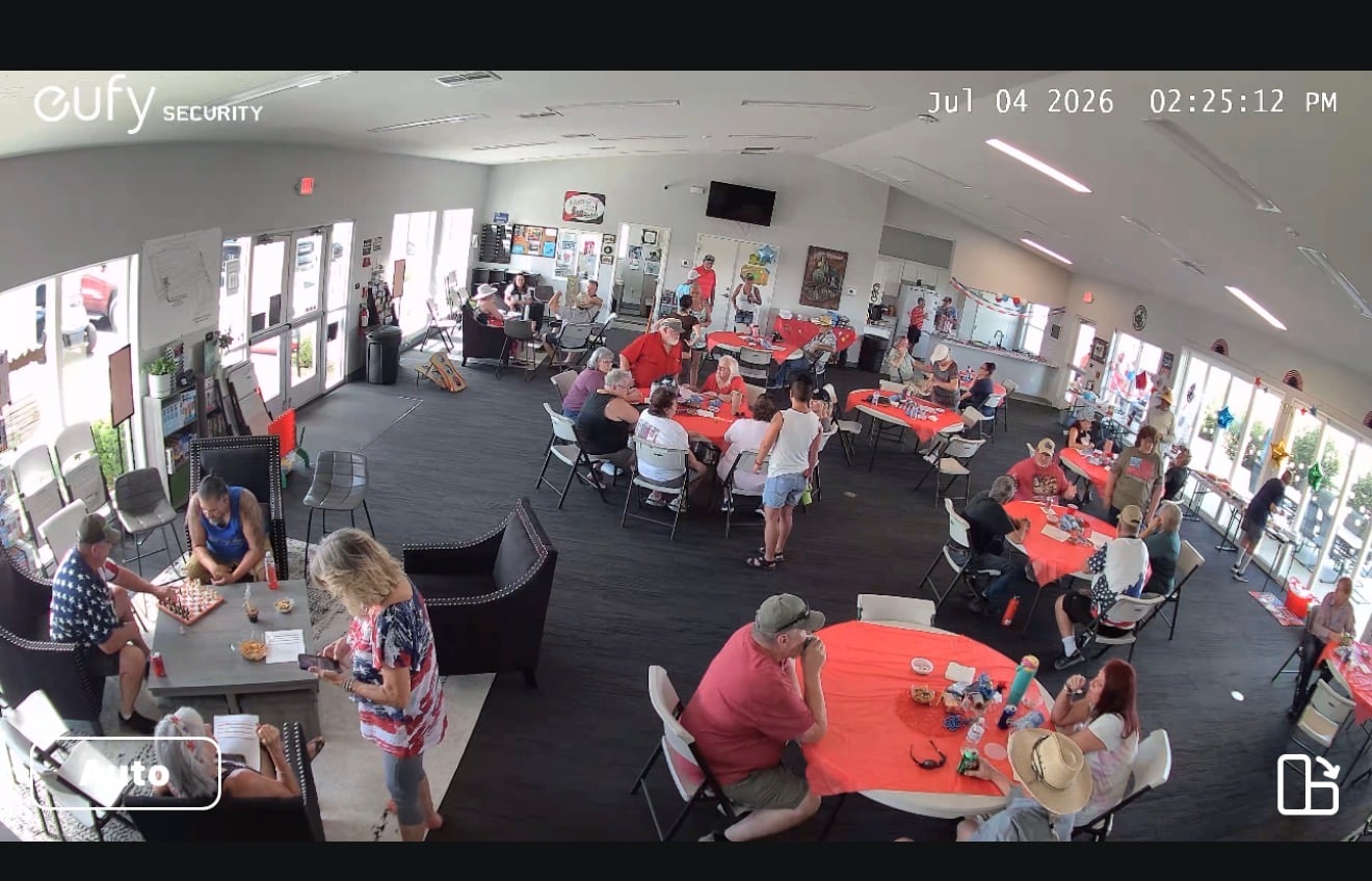 Surveillance footage shows people sitting and standing around tables covered with red tablecloths at an indoor gathering on July 4, 2026.